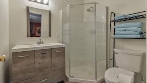 A bathroom with a glass shower enclosure, a white sink, a vanity with wooden drawers, and a towel rack with folded towels. - Eclectic Forest View Efficiency in Quiet Chapel Hill Neighborhood (Chapel Hill)