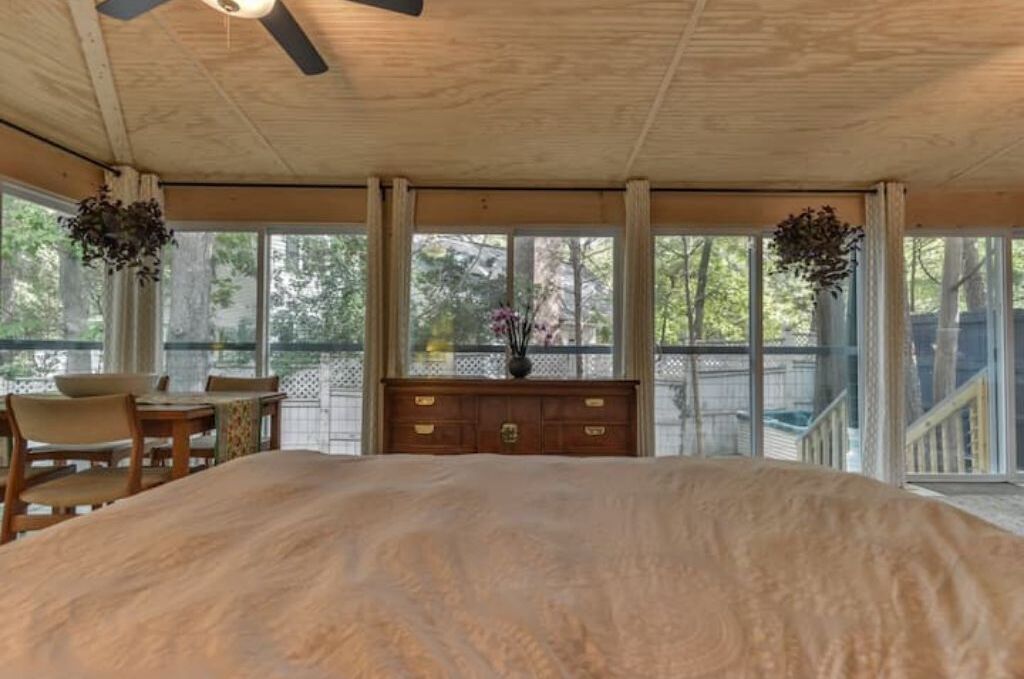 A bedroom with a large bed, a wooden dresser, a desk with chairs, and a ceiling fan.