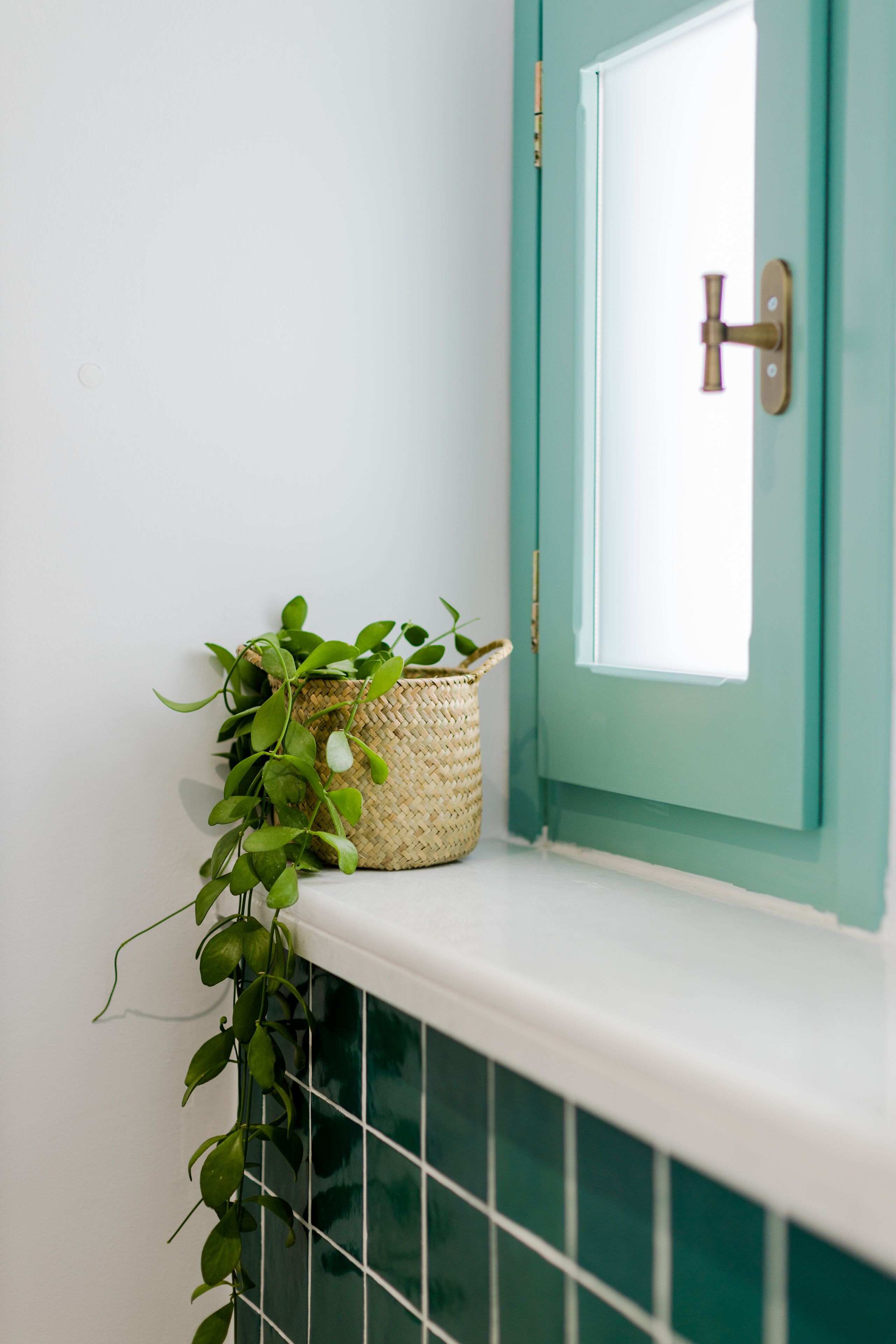 A corner with a teal door, a white tiled wall, and a woven basket with green plants.