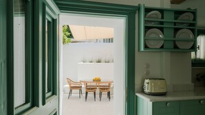 A kitchen with green cabinets, a toaster, and a dining area with wicker chairs and a table. - La Casa Degli Archi (Kos)