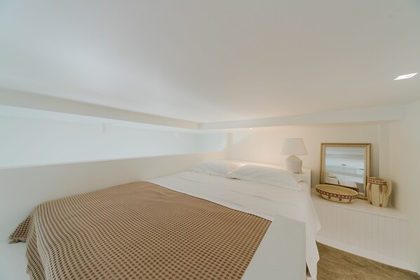 A bedroom with a bed, a bedside table, a lamp, a mirror, and a window.