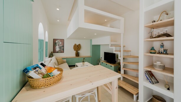 A modern interior with a wooden table, a basket of items, a television, and a bookshelf. - La Casa Degli Archi (Kos)