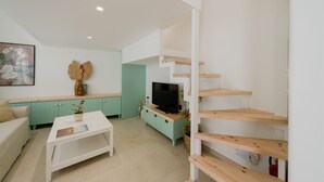 A modern living room with a white sofa, a coffee table, a TV on a wooden stand, and a teal cabinet. - La Casa Degli Archi (Kos)