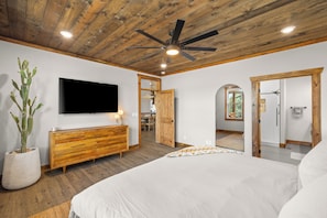 Una camera da letto con un letto grande, soffitto in legno, ventilatore a soffitto, televisione e una pianta in vaso.