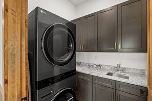 Cocina moderna y funcional, con lavadora y secadora integradas, armarios de madera oscura y encimera de mármol.