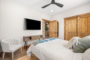 A bedroom with a bed, a chair, a TV, wooden doors, and a ceiling fan.
