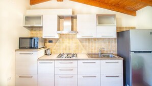 Una cucina compatta con mobili bianchi, un forno a microonde, un piano cottura a gas e un frigorifero in acciaio inossidabile.