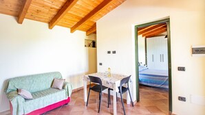 Una stanza con soffitto in legno, un divano verde, un tavolo con sedie e un letto sullo sfondo.