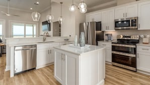 Una cucina moderna con mobili bianchi, elettrodomestici in acciaio inossidabile e illuminazione a sospensione.
