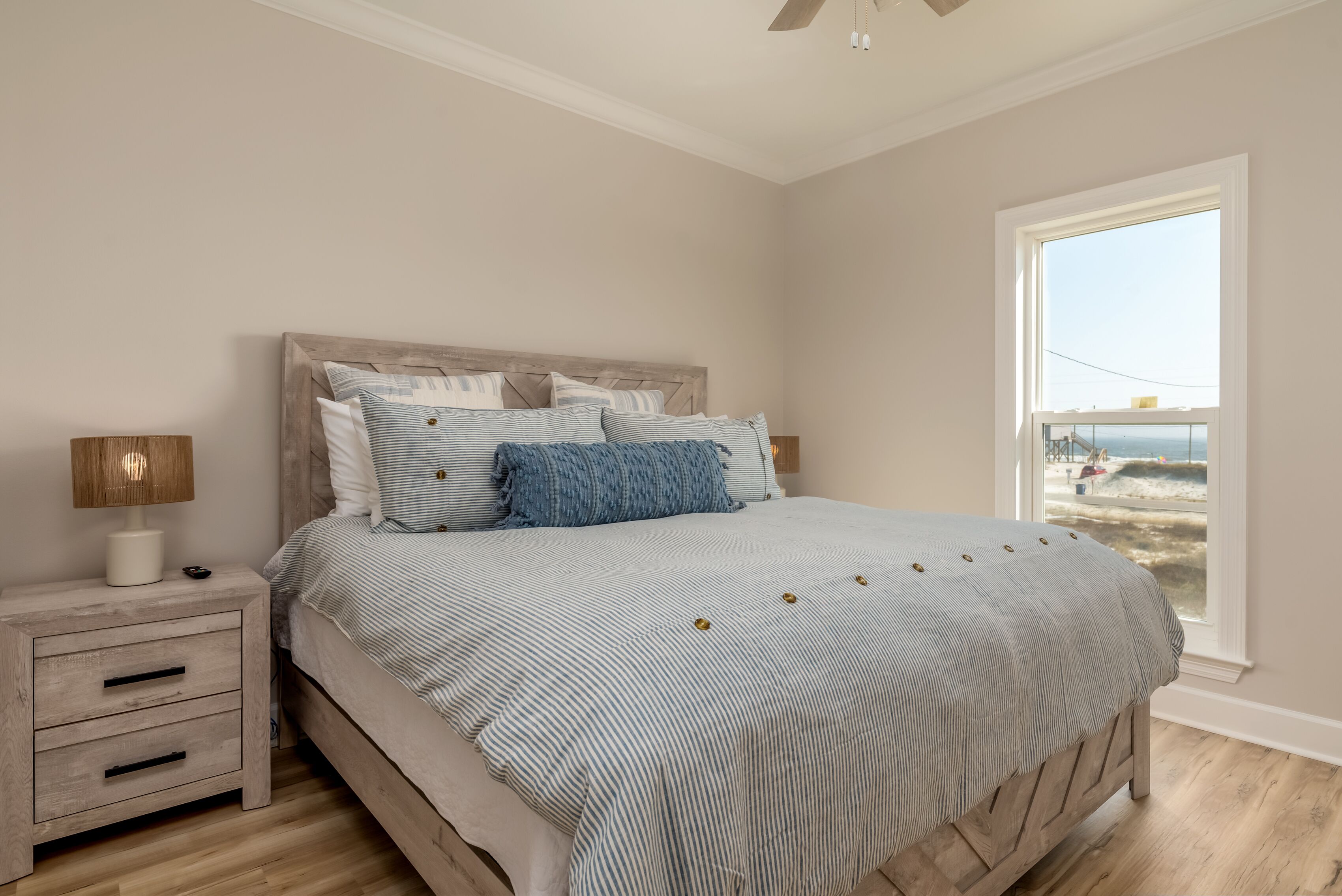 Une chambre à coucher avec un lit, une table de chevet, une lampe et une fenêtre donnant sur la plage.