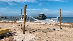Una spiaggia con un'amaca, pali di legno e una piccola struttura su palafitte.