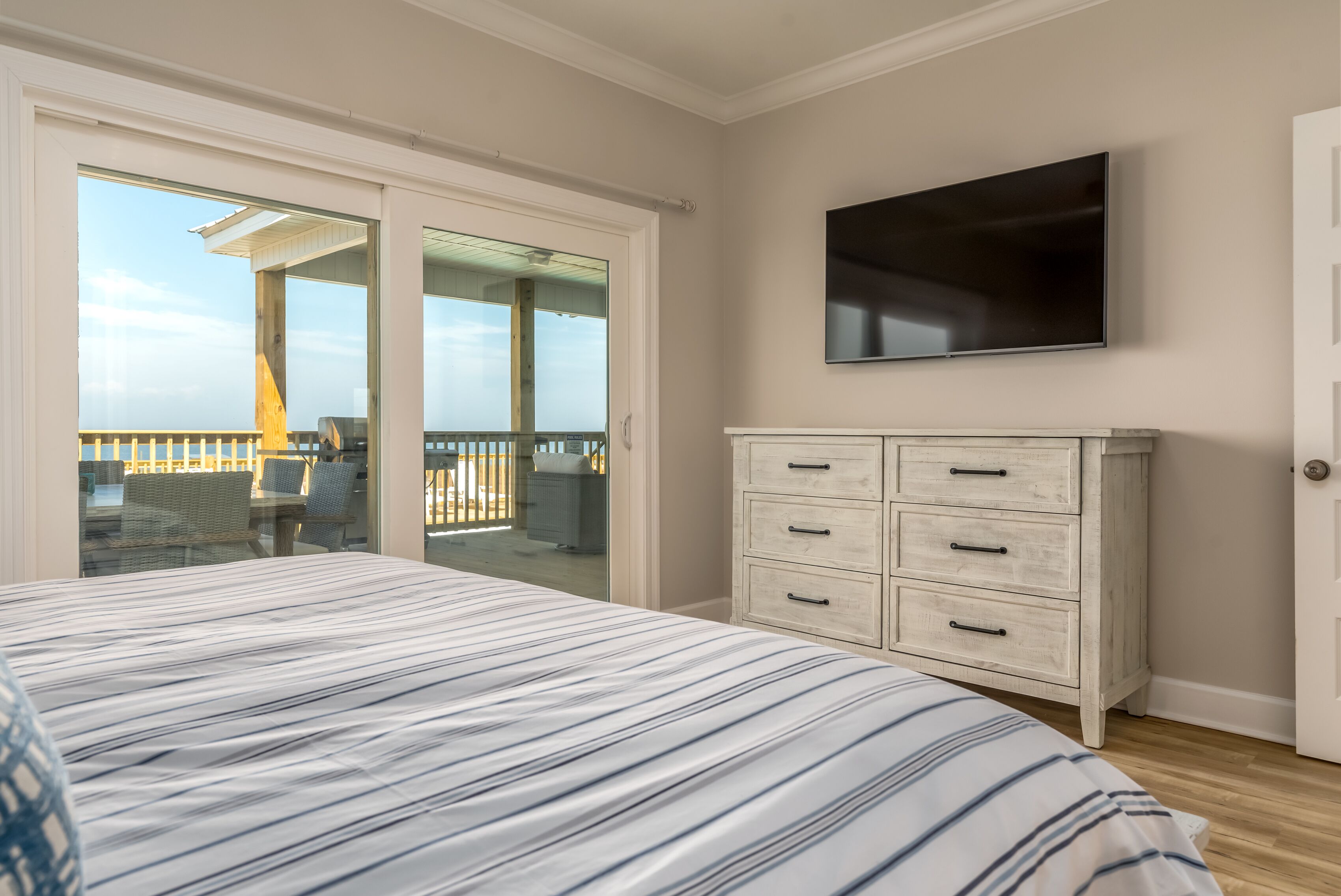 A bedroom with a bed, a dresser, a TV, and a balcony with outdoor furniture.