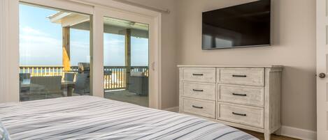 A bedroom with a bed, a dresser, a TV, and a balcony with outdoor furniture.