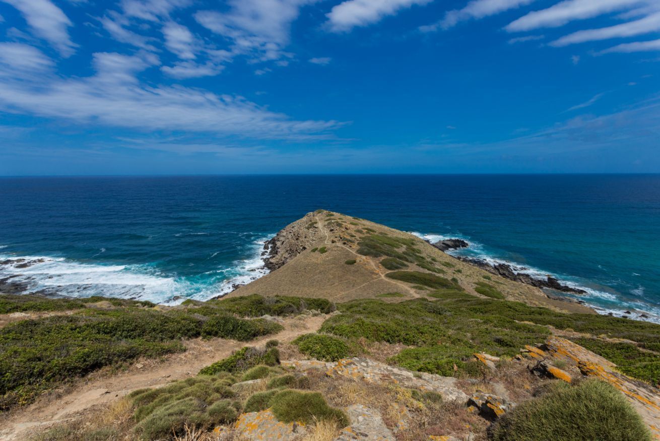 A coastal landscape with a prominent rocky hill and a clear view of the ocean.