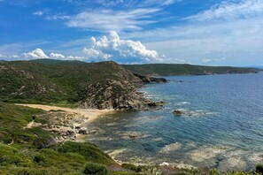 A coastal landscape with a sandy beach, rocky outcrops, and lush greenery.