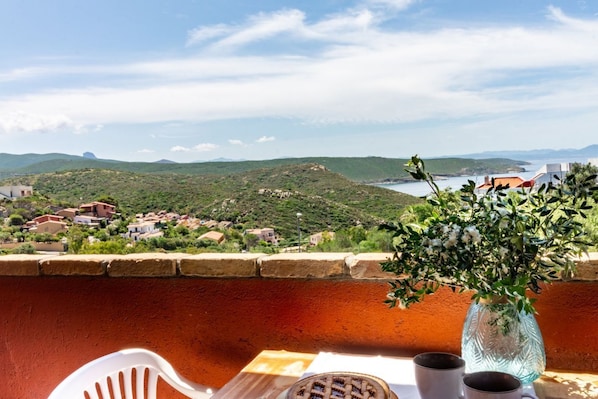 A balcony with a table, two cups, and a vase with flowers.