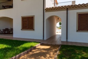 Un bâtiment doté d’un patio couvert, de volets en bois et d’un petit espace extérieur aménagé pour s’asseoir.