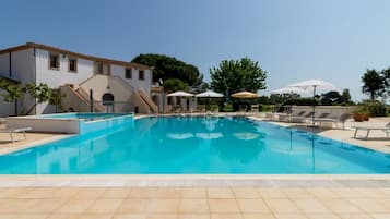 A swimming pool with lounge chairs and umbrellas, surrounded by a building with a tiled roof.