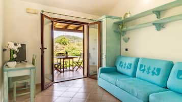 A room with a teal sofa, a small table with a plant, and a view of a patio with a table and chairs.