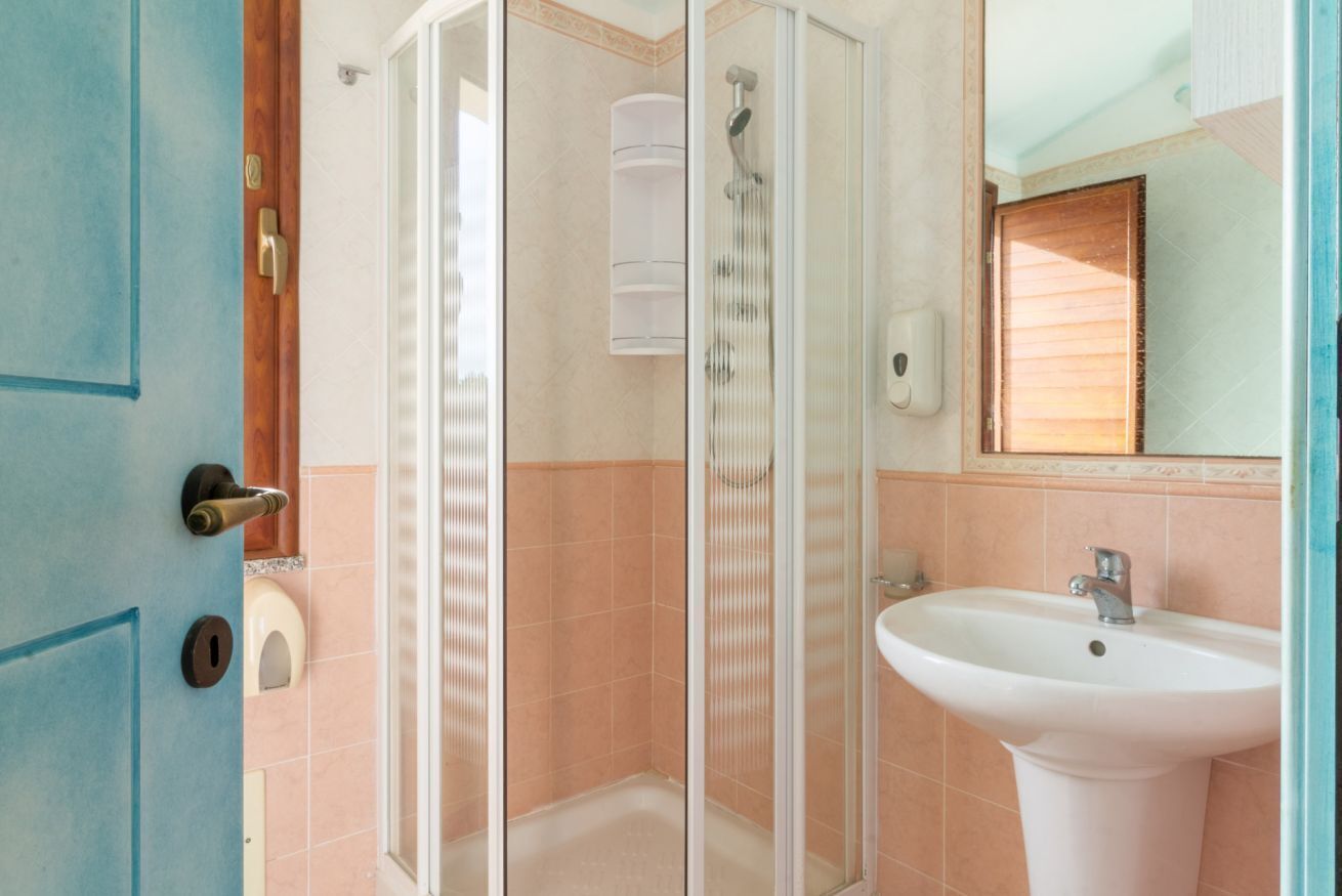 Un bagno con cabina doccia in vetro, un lavandino bianco e uno specchio sopra.