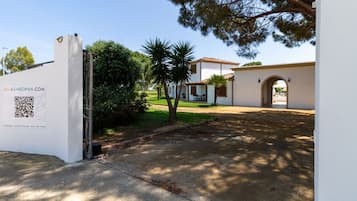 A gated entrance to a property with a white facade, a QR code, and a sign for holiday rental houses and services.