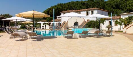A pool area with tiled flooring, sun loungers, and umbrellas.