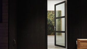 A modern interior with a wooden floor, a large glass door leading outside, and a small wooden bench.