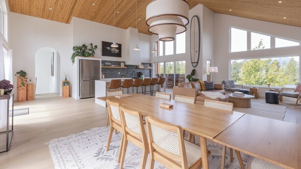 A spacious kitchen with modern appliances, a dining area with a wooden table and chairs, and a view of the outdoors through large windows.