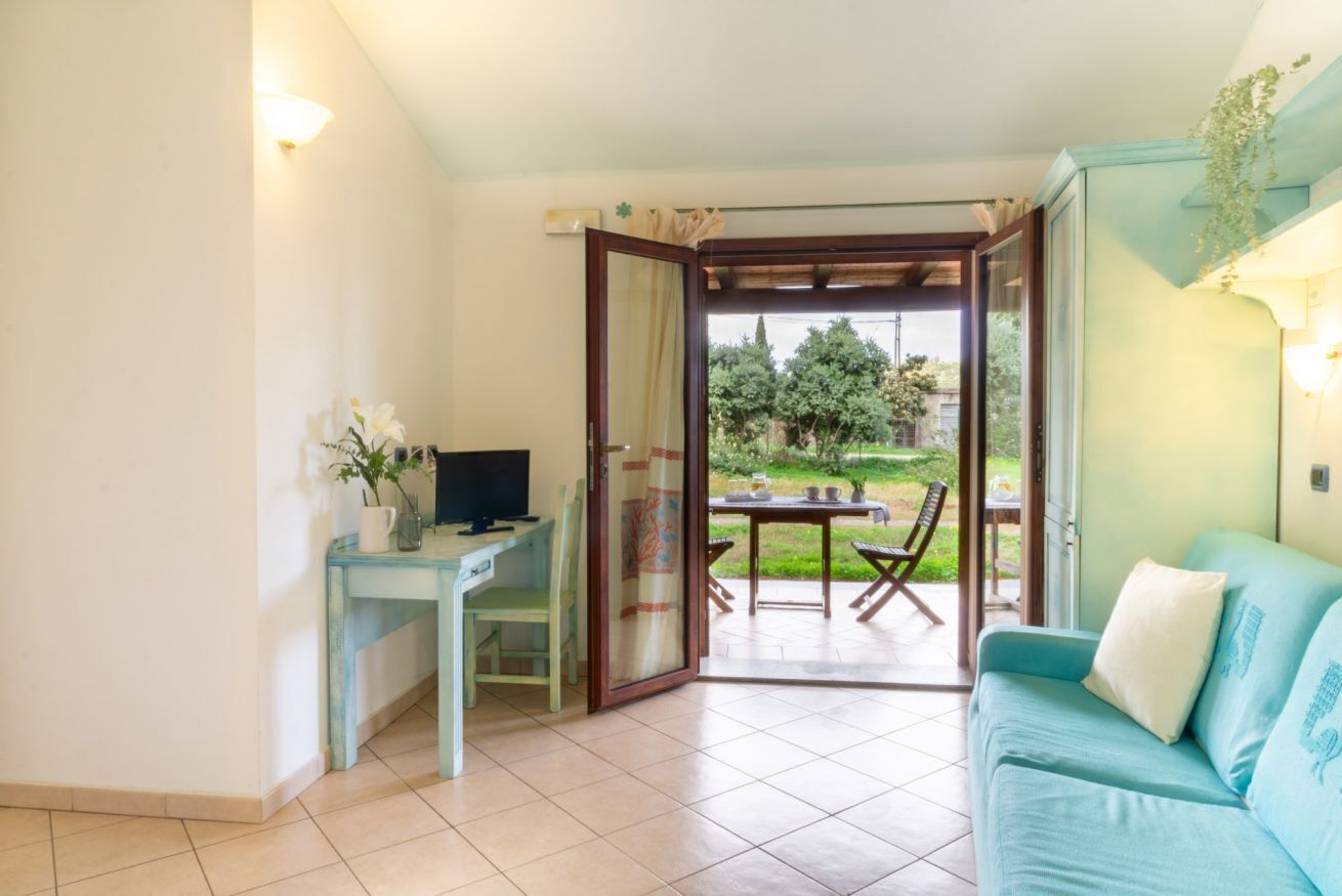 A room with a desk, a computer, a sofa, and a sliding glass door leading to an outdoor area with a table and chairs.