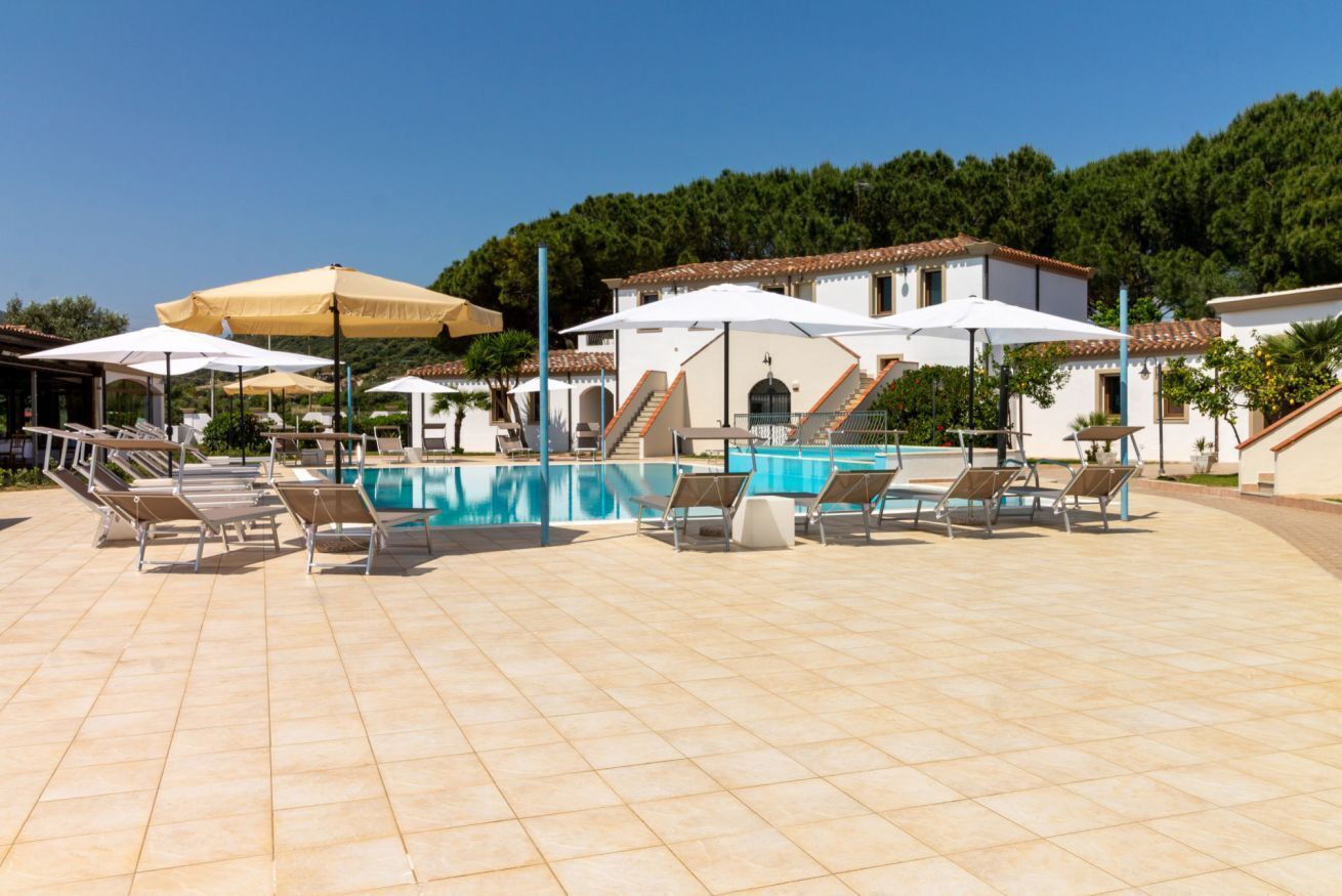 A pool area with tiled flooring, sun loungers, and umbrellas.