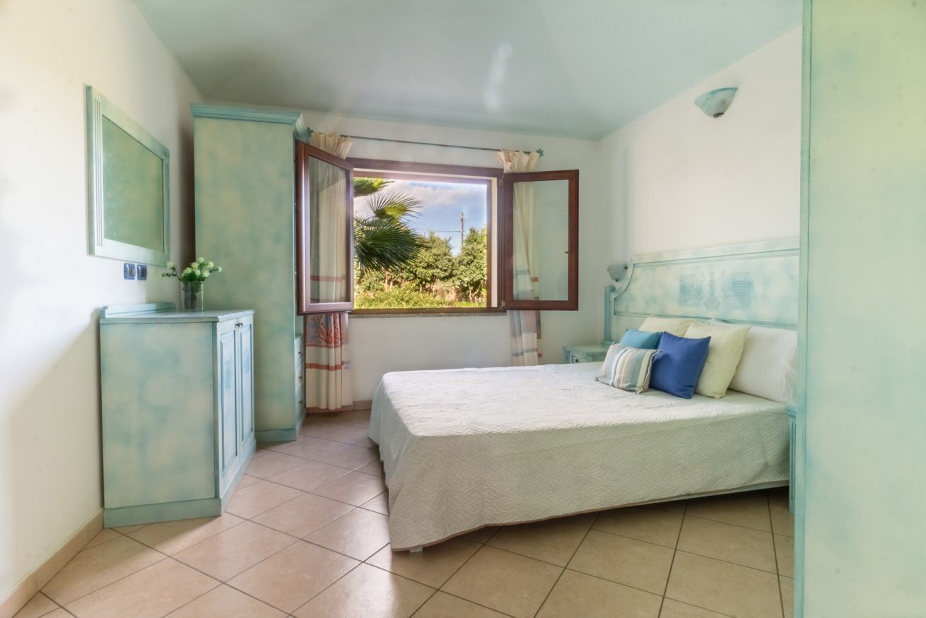 A bedroom with a bed, a window with curtains, a mirror, and a cabinet.