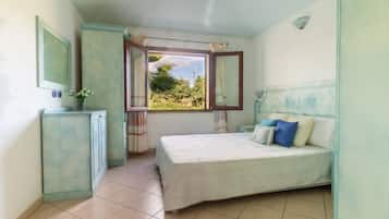 A bedroom with a bed, a window with curtains, a mirror, and a cabinet.