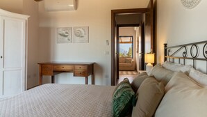 Ein Schlafzimmer mit einem Bett, einem Schreibtisch und einem Nachttisch. Eine Tür führt in einen anderen Raum.