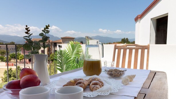 Ein Tisch mit Gebäck, ein Saftkrug und eine Schüssel mit Früchten auf einem Balkon mit Blick auf Berge.