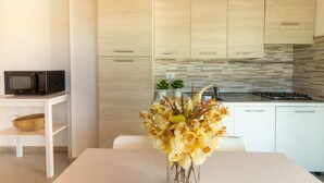 A modern kitchen with light wood cabinets, a microwave on a white shelf, and a vase of yellow flowers on the table. - Sole Apartment by All4sardinia  (Arbatax)