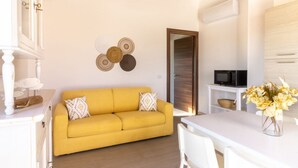 A yellow sofa with patterned cushions, a white dining table, and a vase of flowers. - Sole Apartment by All4sardinia  (Arbatax)