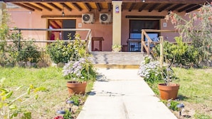 A rustic building with a wooden pergola, a concrete pathway, and potted plants.