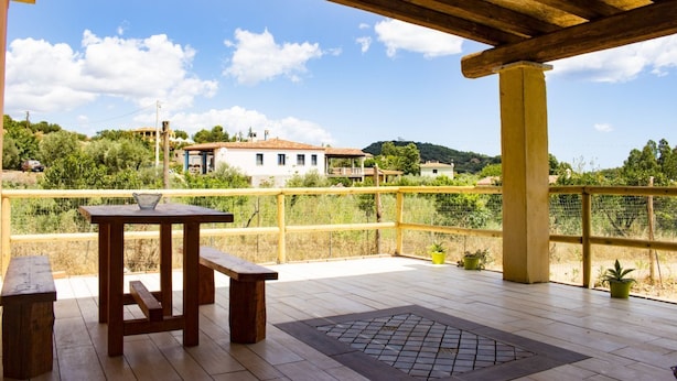 A wooden deck with a table and benches, overlooking a hillside with buildings.
