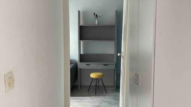 Un couloir étroit mène à une pièce où se trouvent un bureau, des étagères et un tabouret jaune.