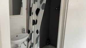 Une salle de bain avec un lavabo blanc, un rideau de douche à motifs à pois et une cabine de douche sombre.