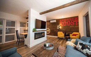 Ein modernes Wohnzimmer mit Kamin, einem Essbereich mit Glastrennwand und einer Wand mit dem Schild 'REDNECK ROOST'.