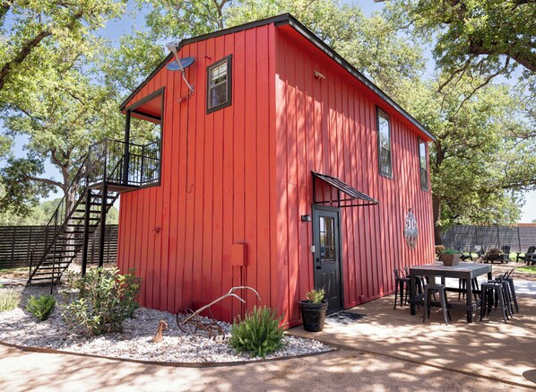 Un bâtiment rouge avec un escalier noir, une porte et un petit jardin agrémenté de plantes et d’une table avec des chaises.