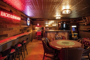 Eine Bar mit Holzwänden, einer Neonreklame, einer Theke, Hockstühlen und einem runden Tisch mit Stühlen.
