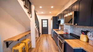 A modern kitchen with wooden flooring, dark cabinets, a stainless steel range hood, and a wooden countertop.