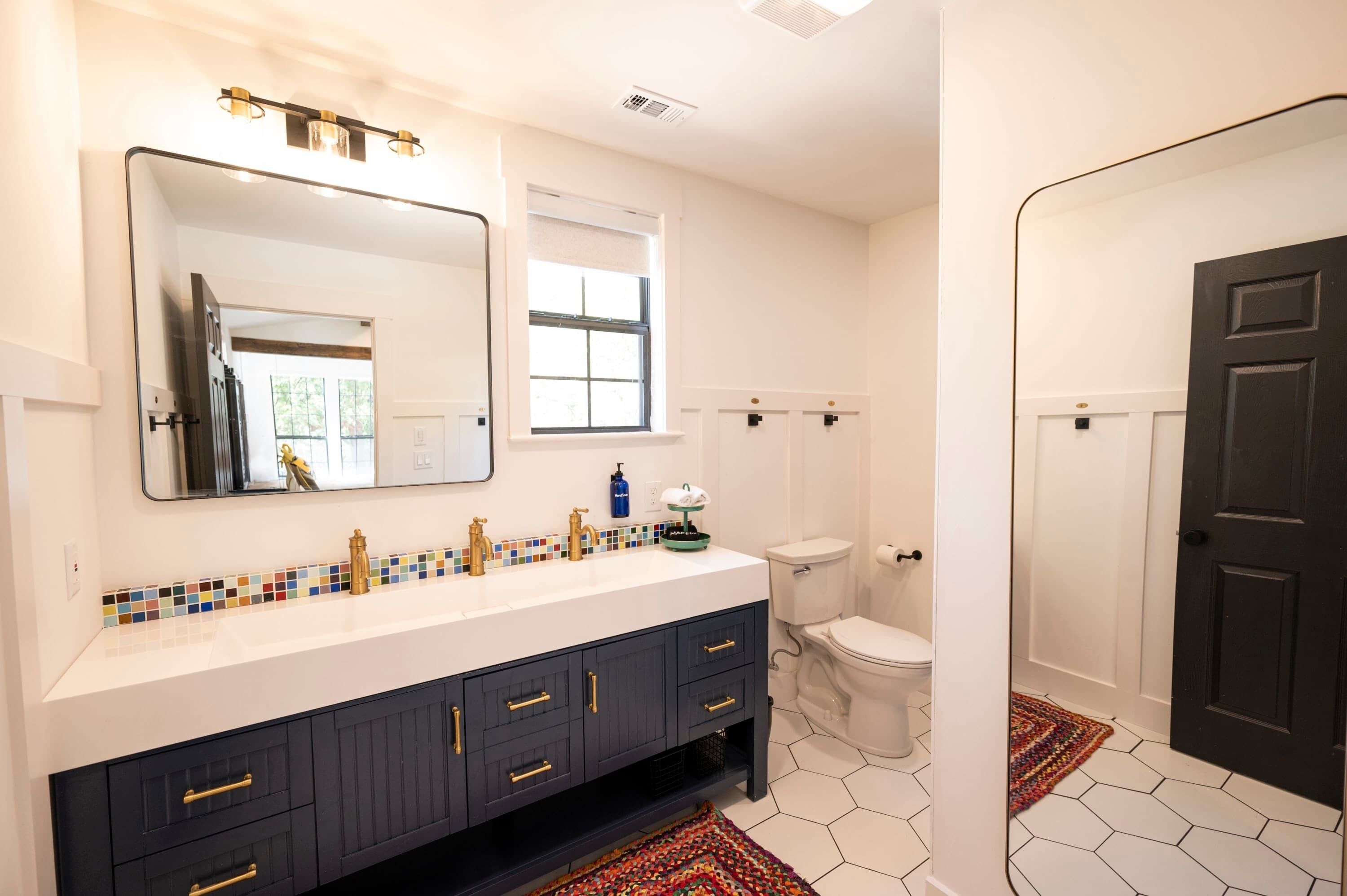 A bathroom with a white sink, black cabinets, a large mirror, a toilet, and a black door.