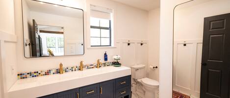 A bathroom with a white sink, black cabinets, a large mirror, a toilet, and a black door.