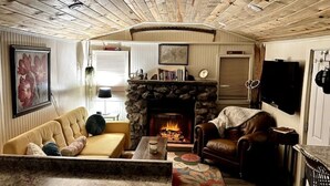 A cozy living room with a stone fireplace, a sofa, a leather armchair, and a television mounted on the wall.