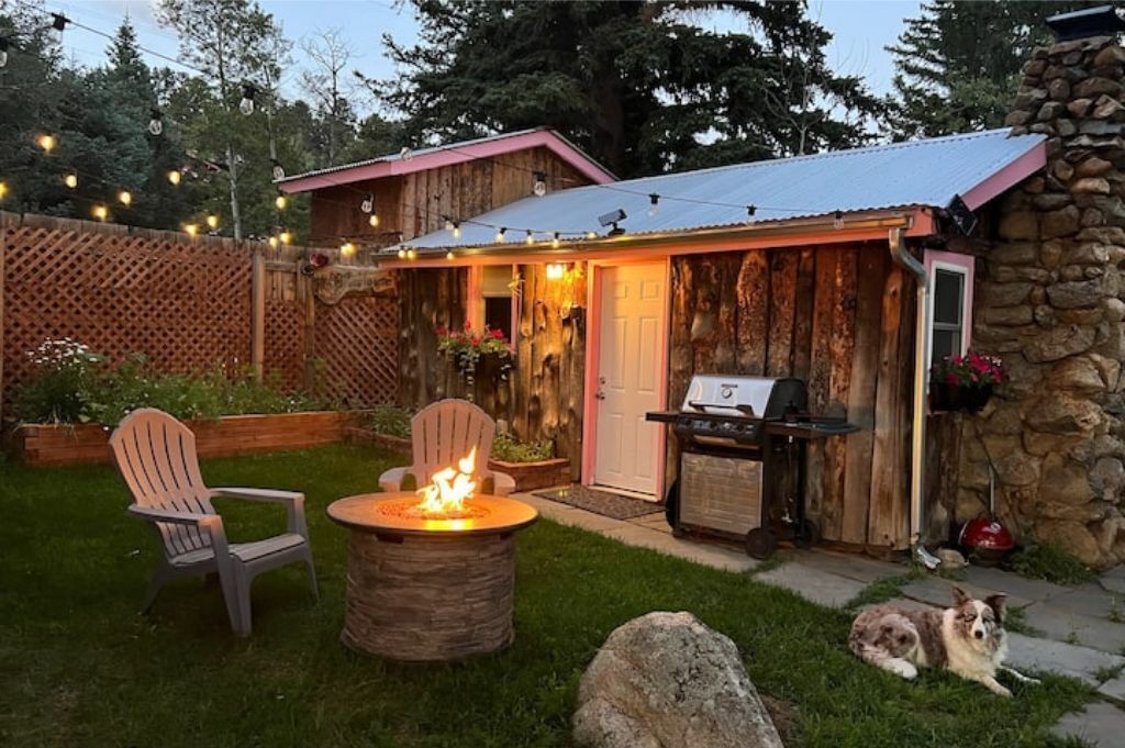 Un jardin avec un foyer, deux fauteuils Adirondack, un barbecue et un chien.