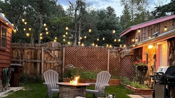A backyard with a fire pit, two Adirondack chairs, a dog, and a wooden fence.