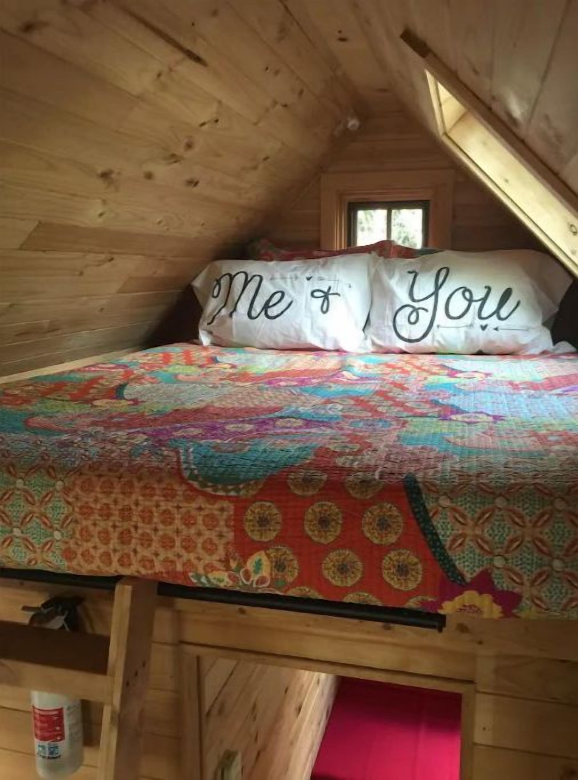 Ein gemütliches Schlafzimmer im Dachgeschoss mit Holzbalkendecke, einer farbenfrohen Steudecke und einem Fenster.